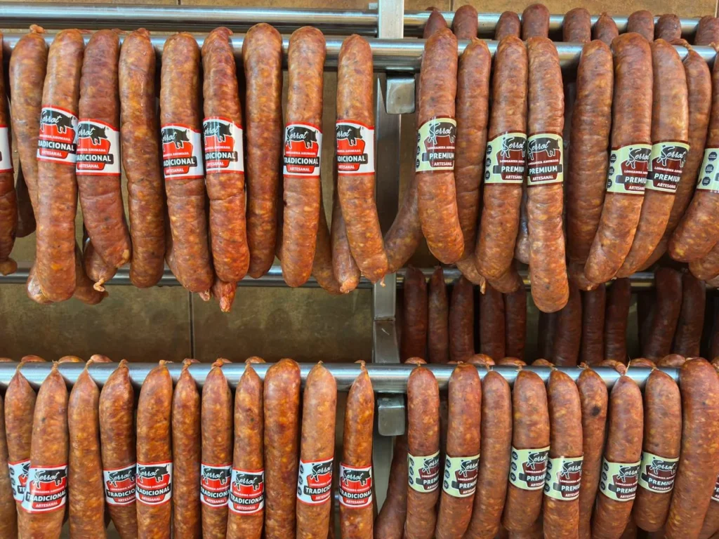 Longanizas Tradicional y Premium Serrot colgadas lado a lado en la sala de ahumado